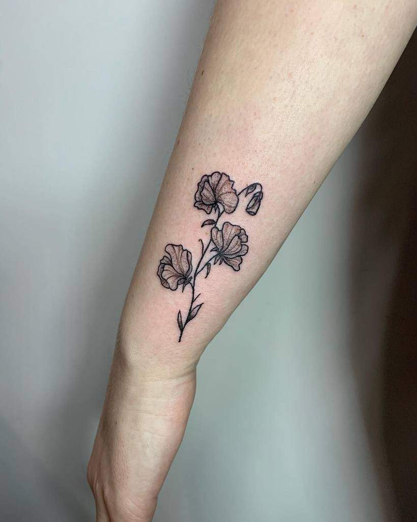 Black and grey sweet pea flower tattoo on the inner wrist, featuring fine line details