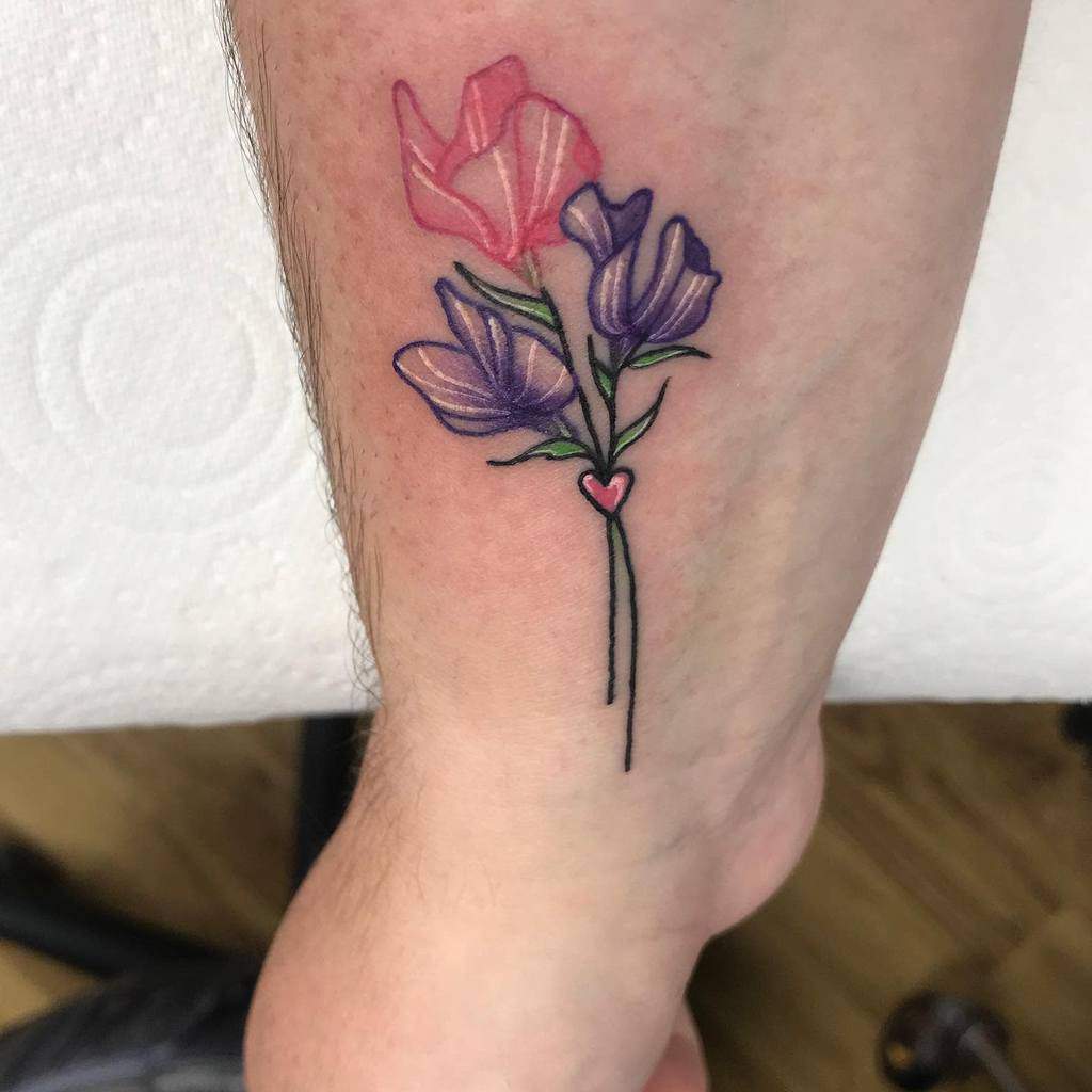 Sweet pea flower tattoo in pink and purple with a small heart detail on the wrist