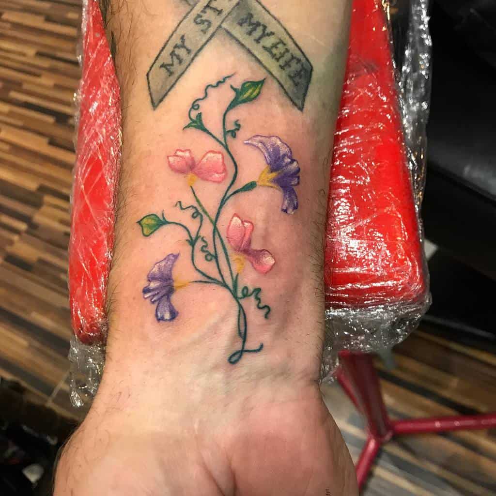 Colorful sweet pea flower wrist tattoo with pink and purple blooms intertwined with green vines