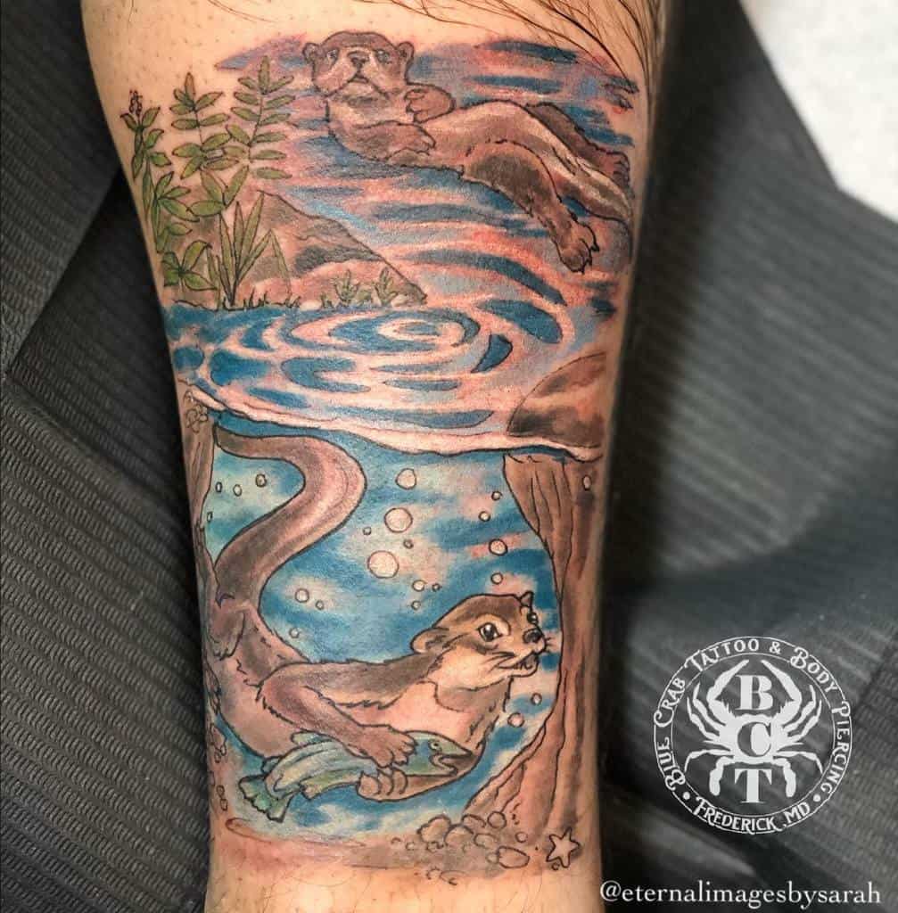 A tattoo of two otters; one playfully swimming with a fish and the other lounging on the riverbank above