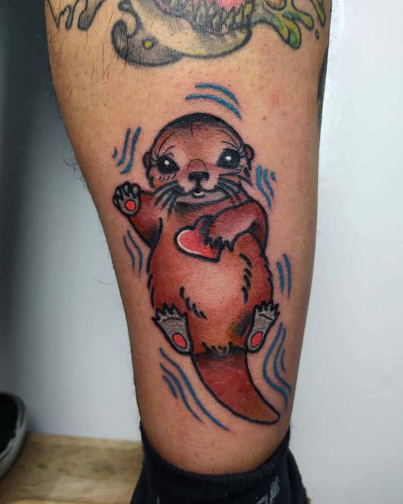 Cartoon otter tattoo on a leg, clutching a red heart with blue waves swirling around it