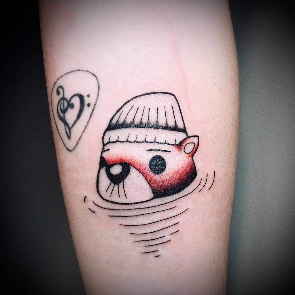 Otter in a beanie, half-submerged with a heart above it, adorns a forearm
