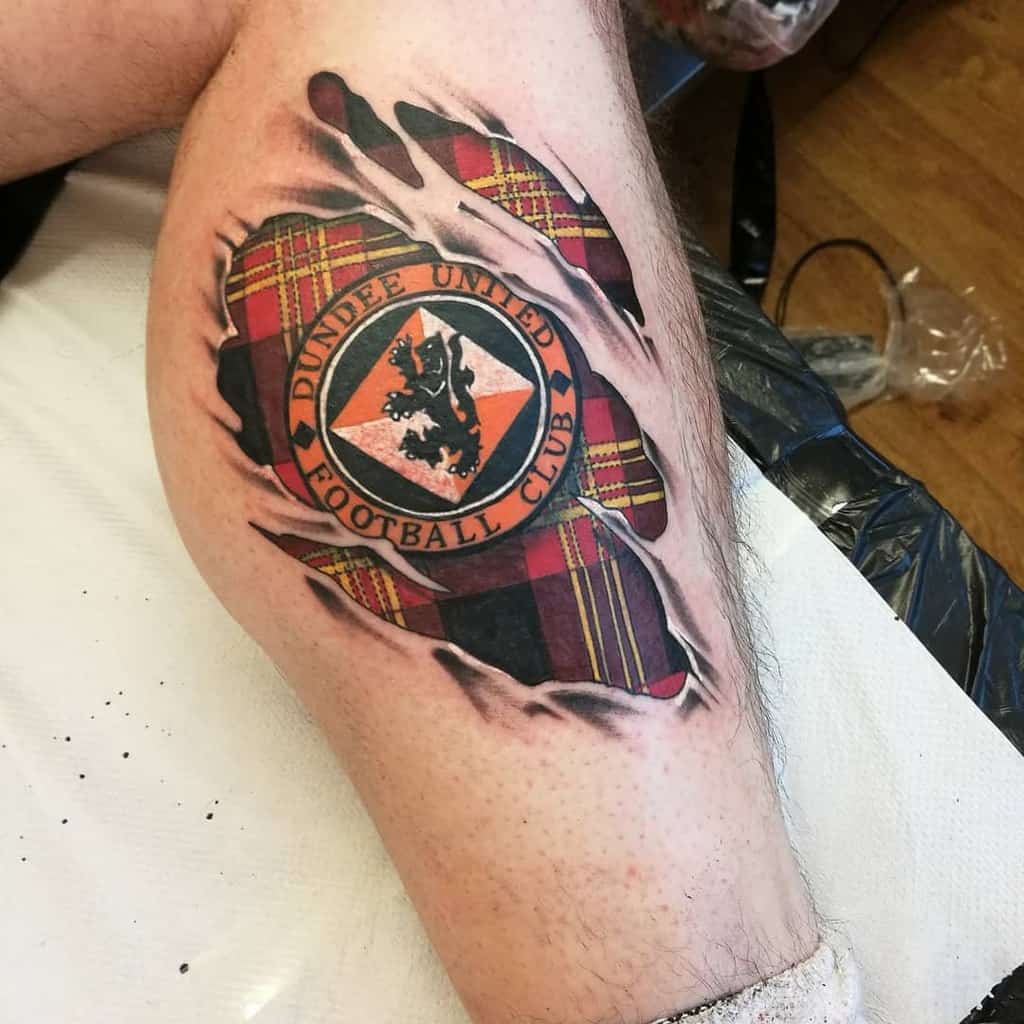 A Scottish tattoo of Dundee United Football Club logo with a tartan pattern background, appearing to tear through the skin