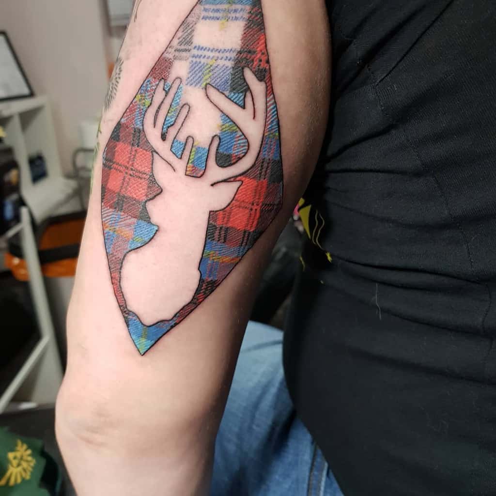 Colorful tattoo of stylized silhouette of a Scottish stag with antlers set against a colorful tartan pattern