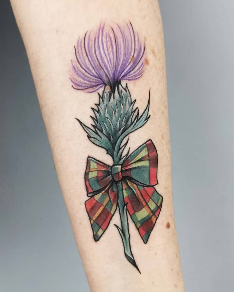 Scottish tattoo of a purple thistle with a green stem and a red, green, orange plaid bow