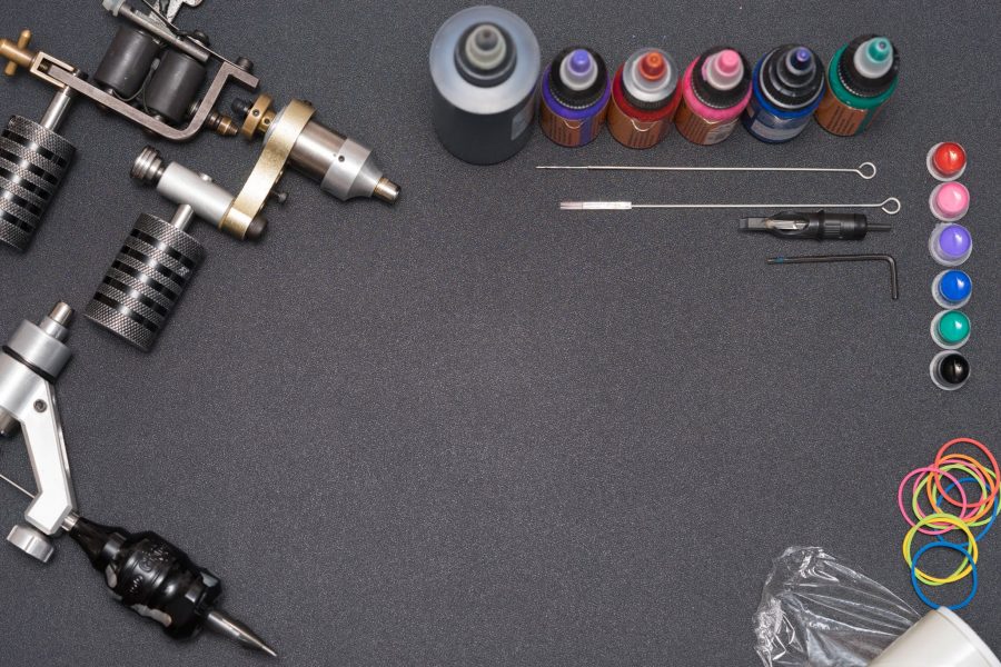Tattoo equipment including machines, ink bottles, single needle sets, needles, and colored caps on a dark surface
