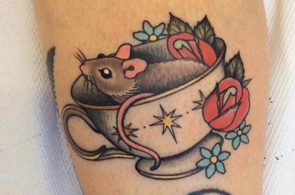 Colorful tattoo of a mouse inside a teacup adorned with stars, surrounded by red roses and blue flowers