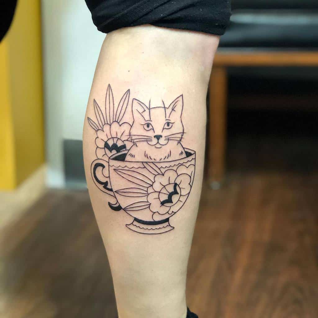 Line art tattoo of a cat in a floral teacup, featuring flowers and leaves around the cup