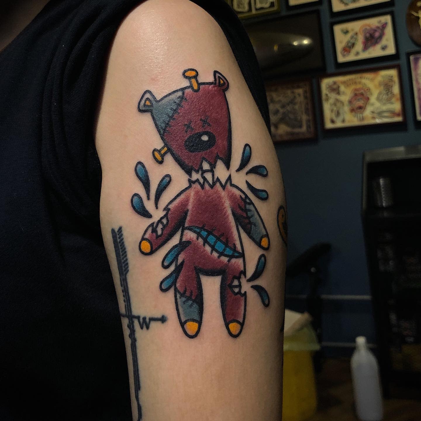 Tattoo of a crying, stitched-up red teddy bear on someone's upper arm