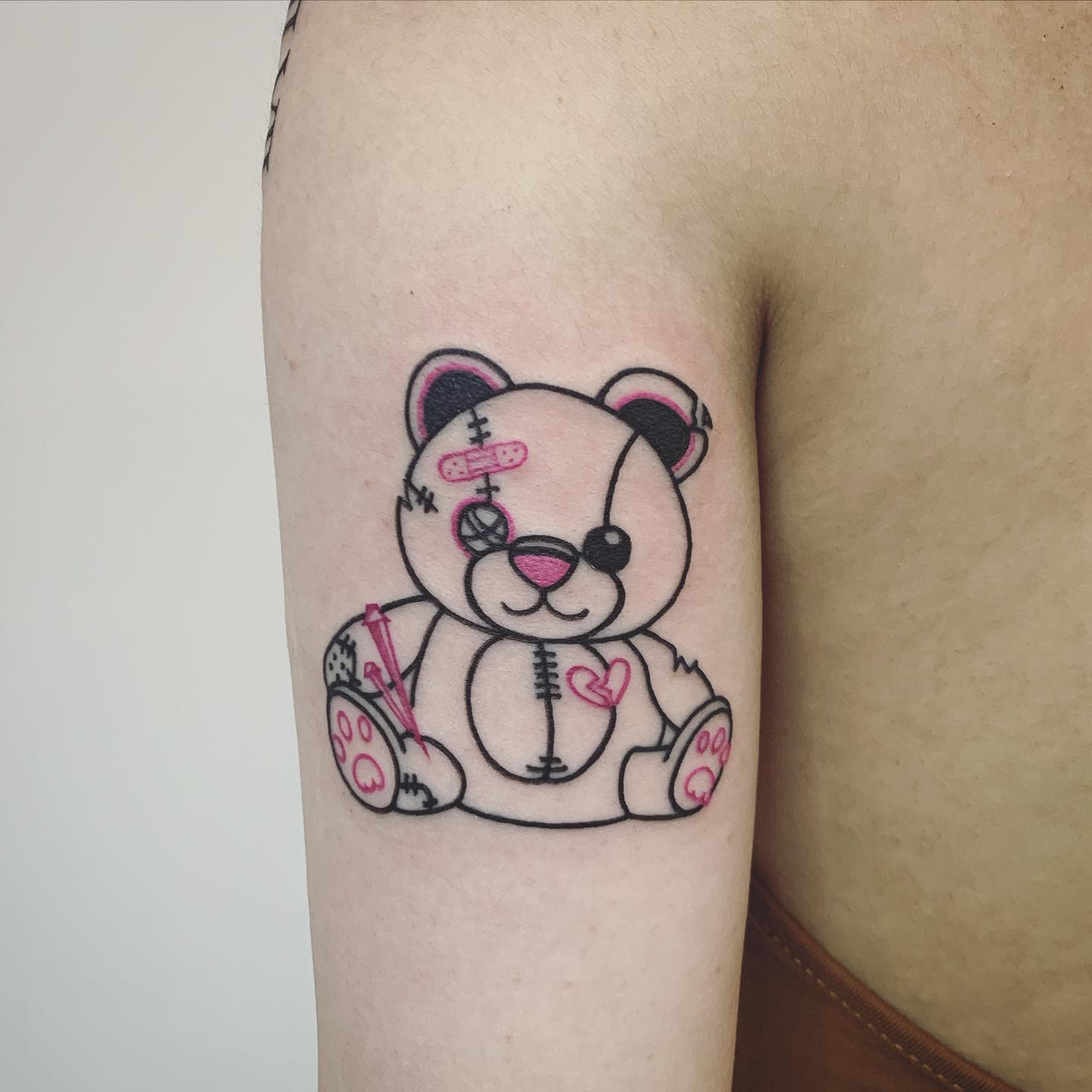 Tattoo of a stitched teddy bear with bandages and a pink heart on an arm