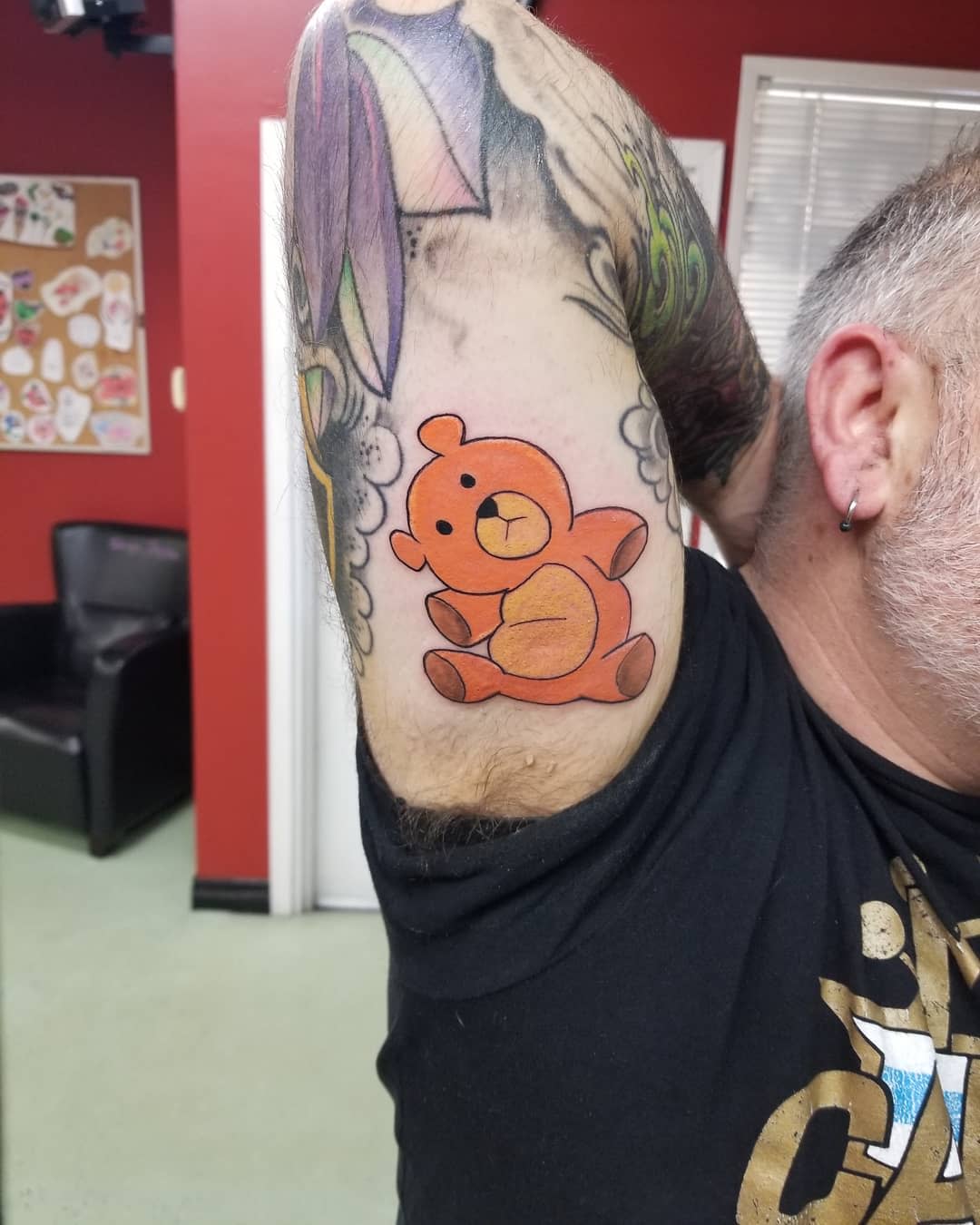 A brightly colored teddy bear tattoo on an upper arm