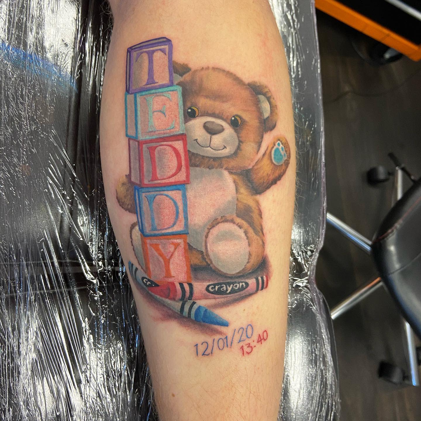 Tattoo of a teddy bear with building blocks spelling "TEDDY" and crayons, dated 12/01/20 13:40