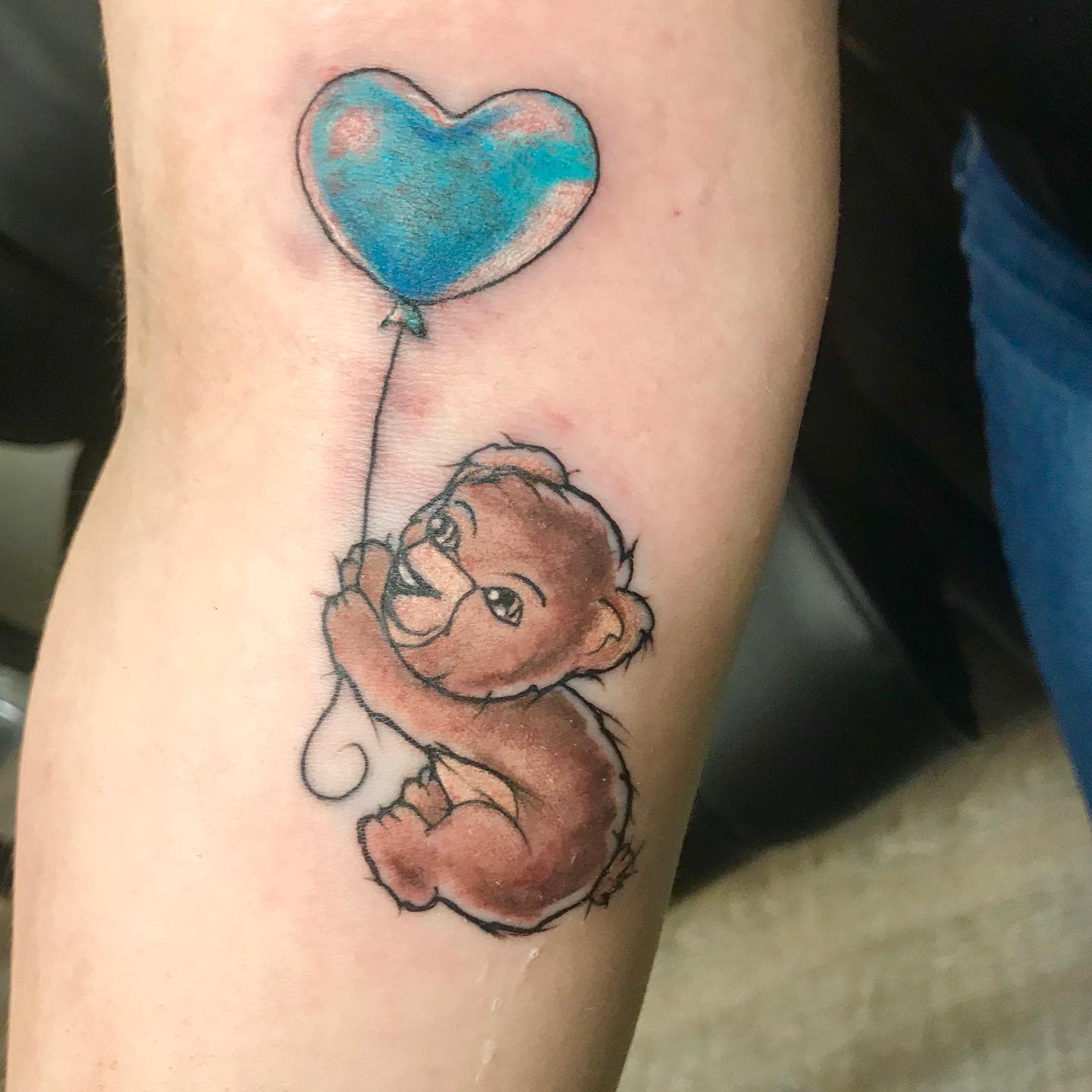Tattoo of a teddy bear holding a blue heart-shaped balloon on an arm