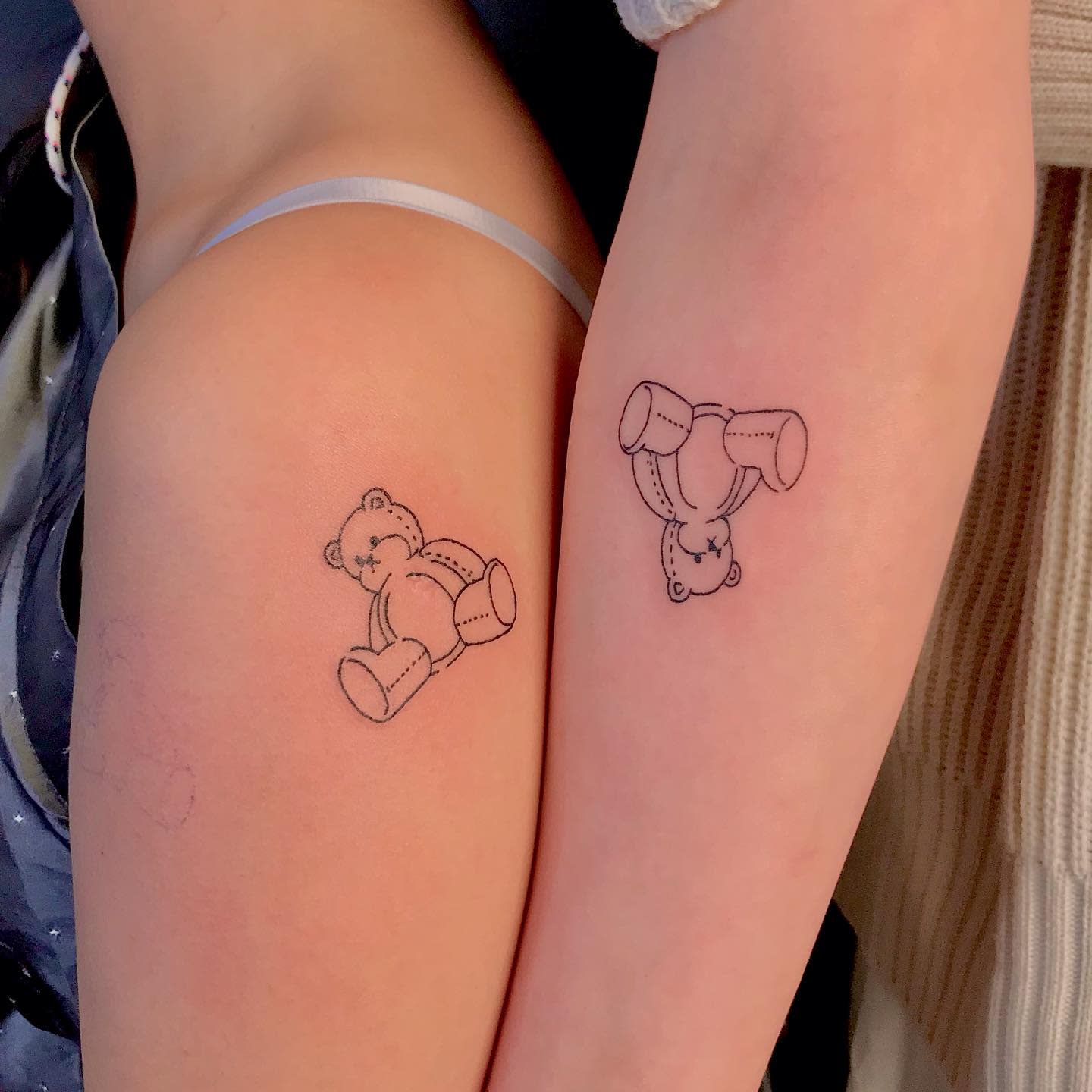 Two arms with matching teddy bear outline tattoos, one upright and one upside down