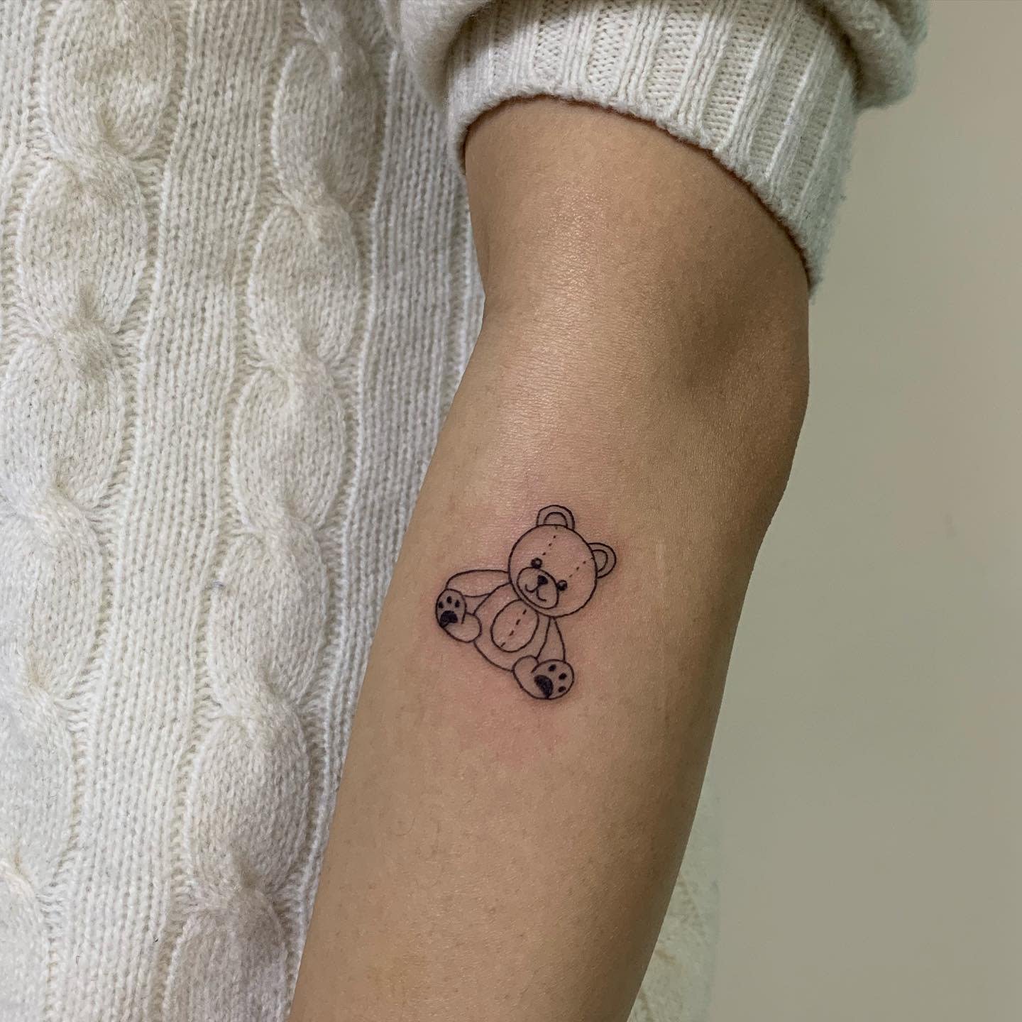 A small teddy bear outline tattoo on the inner arm