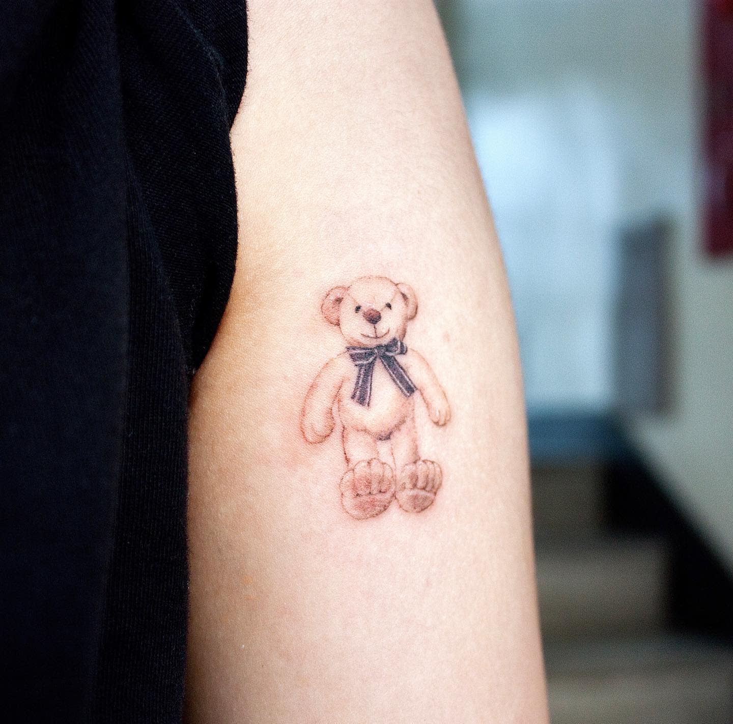 Tattoo of a teddy bear with a bow on the upper arm