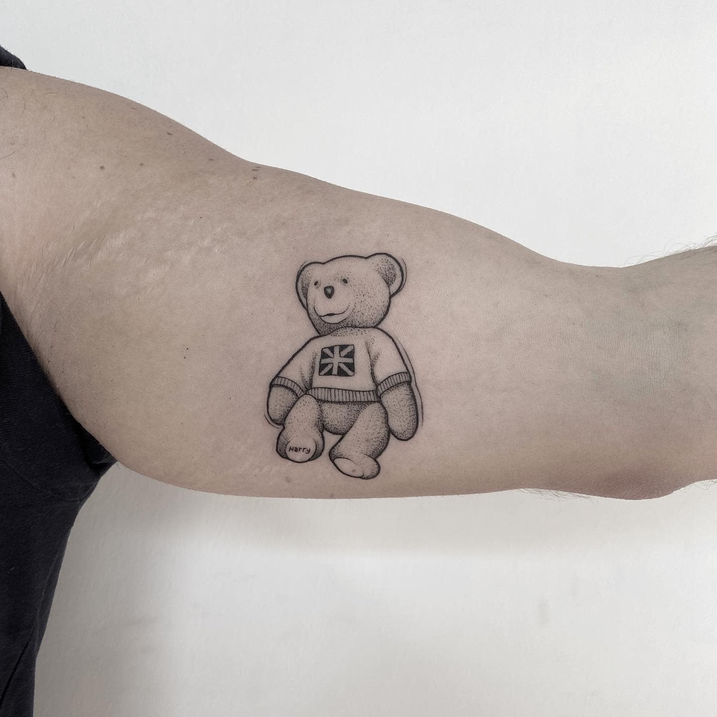 Tattoo of a teddy bear with a Union Jack sweater on a bicep