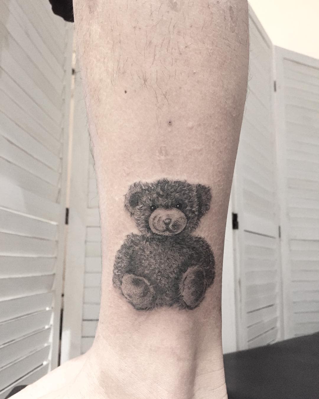 A tattoo of a teddy bear on the lower part of a leg near the ankle