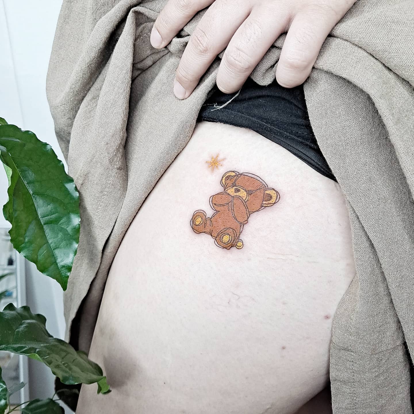 A cute teddy bear tattoo with a star on an upper thigh