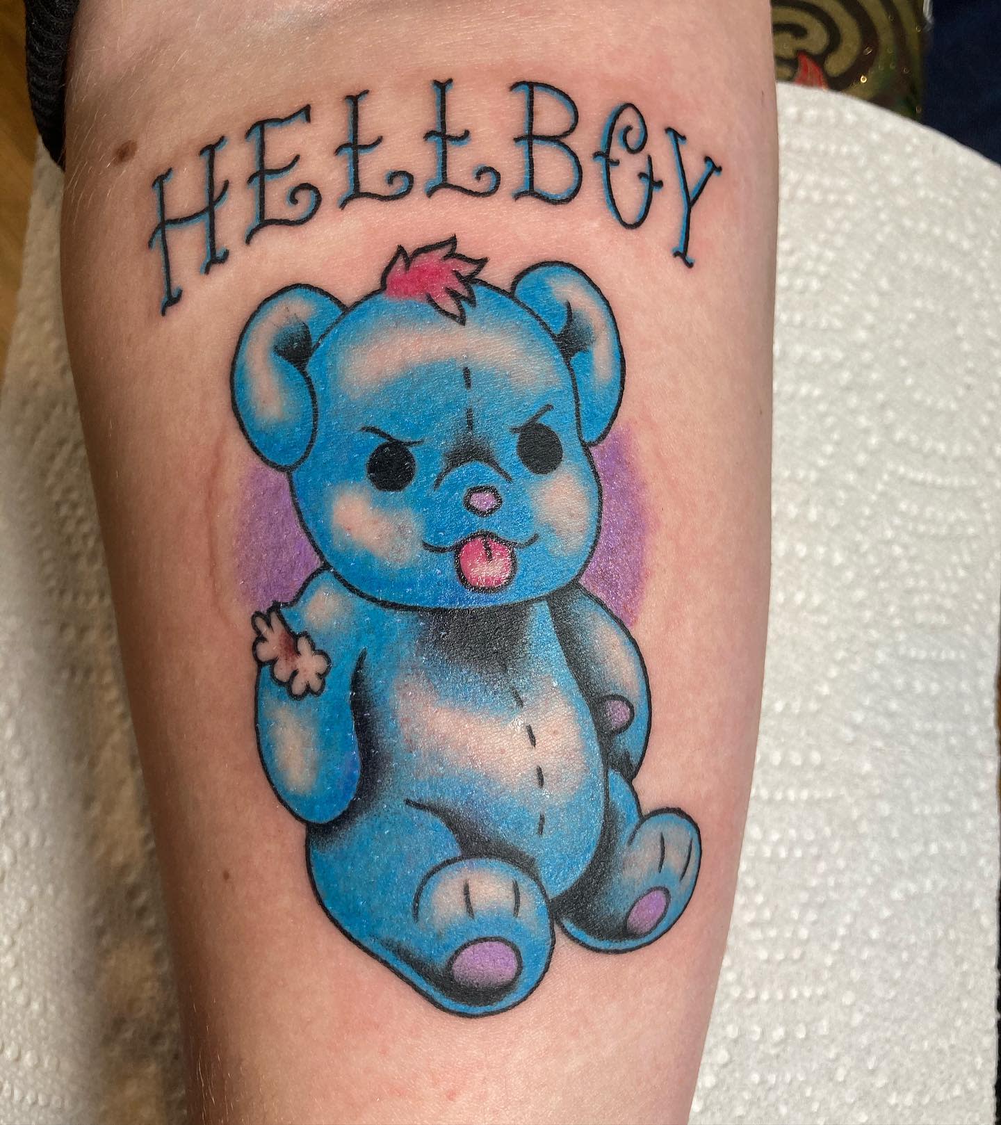 Colorful teddy bear tattoo with the word "Hellboy" above it, featuring pink details on the bear
