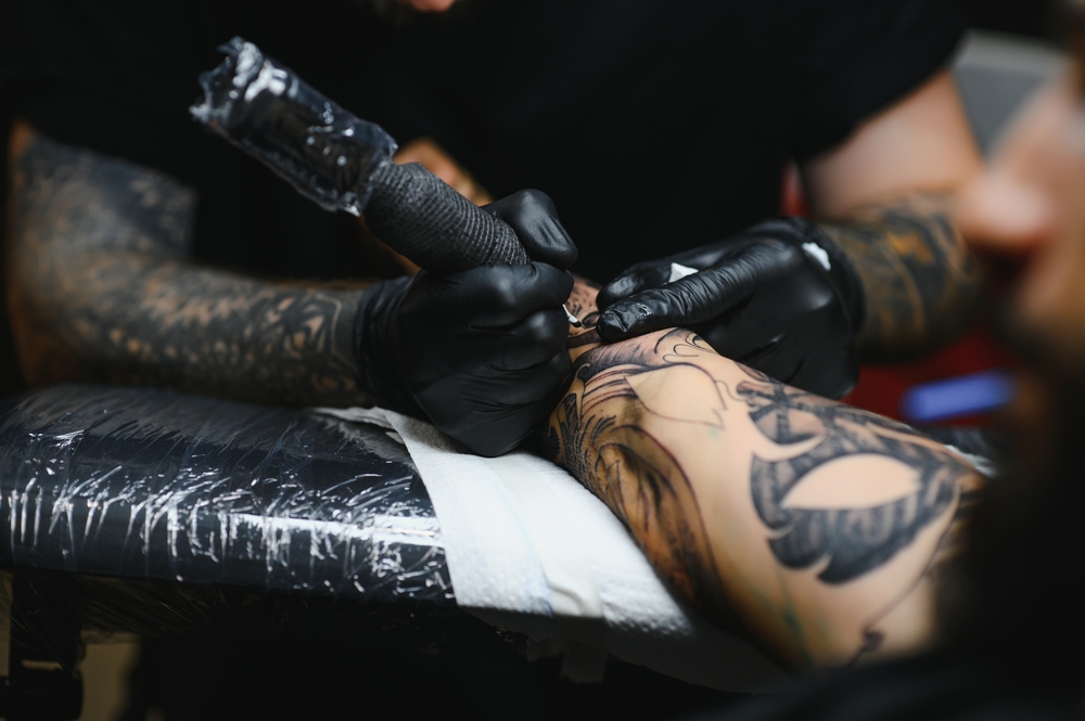 Tattoo artist wearing black gloves works on a detailed forearm tattoo, concentrating on quality options for different tattoo budgets