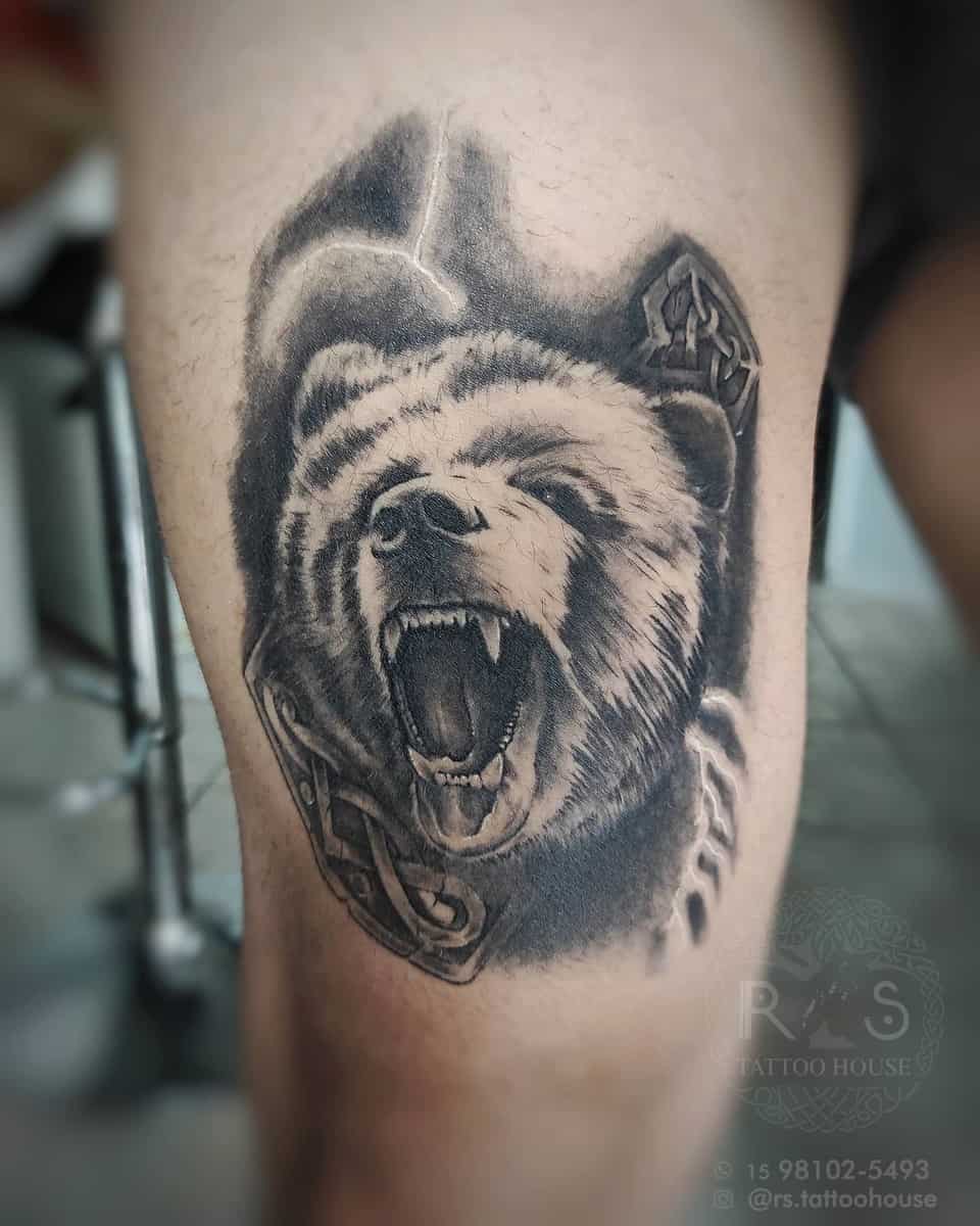 Tattoo of a fierce bear head roaring, adorned with intricate Norse symbols, perfect for the arm or leg