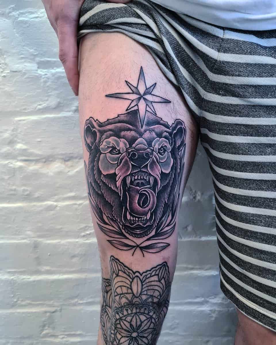 Tattoo of a roaring bear on a man's thigh, featuring a star above and intricate geometric patterns below