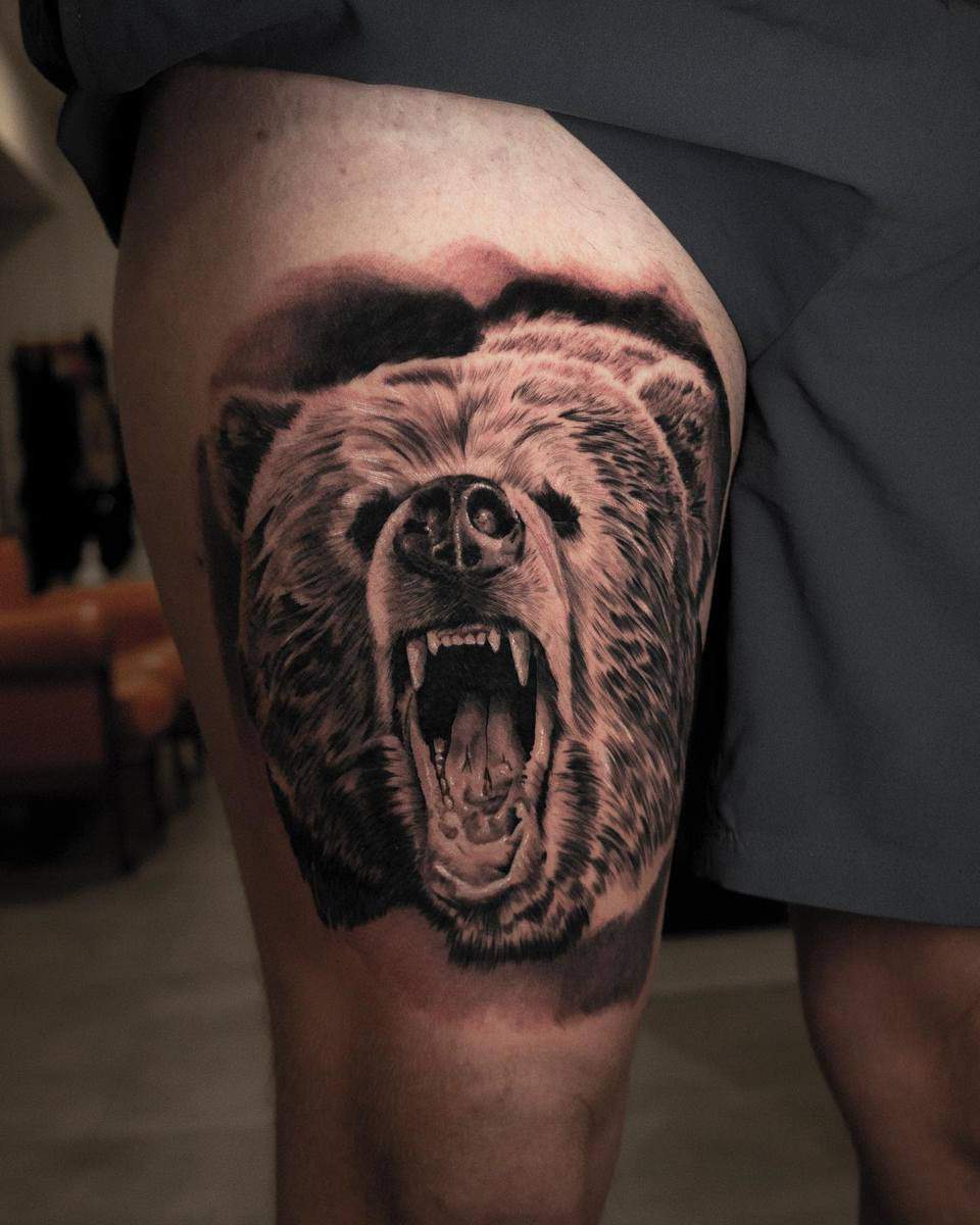 Tattoo of a roaring bear on a person's upper thigh with detailed shading and an incredibly realistic style