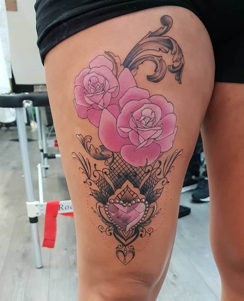 Chandelier-style thigh tattoo featuring pink roses, ornate filigree, lace details, and a heart-shaped pendant with beaded accents
