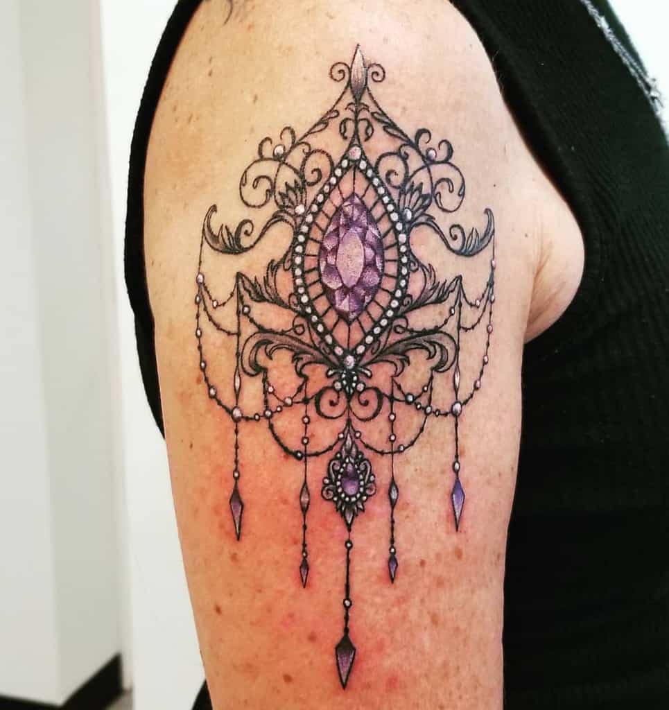 Chandelier-style tattoo with an ornate filigree design, a large purple gemstone centerpiece, delicate beaded chains, and diamond-shaped crystal accents