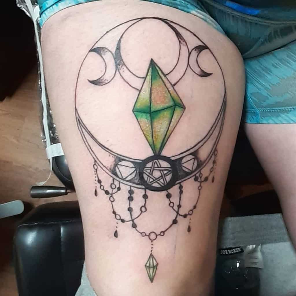 Chandelier-style tattoo featuring a green crystal, crescent moons, a pentacle, beaded chains, and a dangling diamond crystal accent
