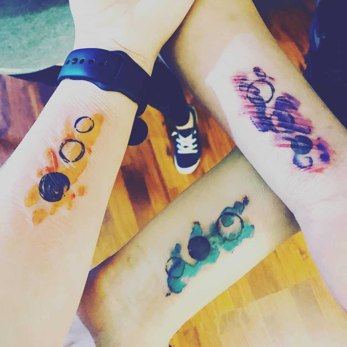 Three colorful matching tattoos on arms with circles and splashes of ink