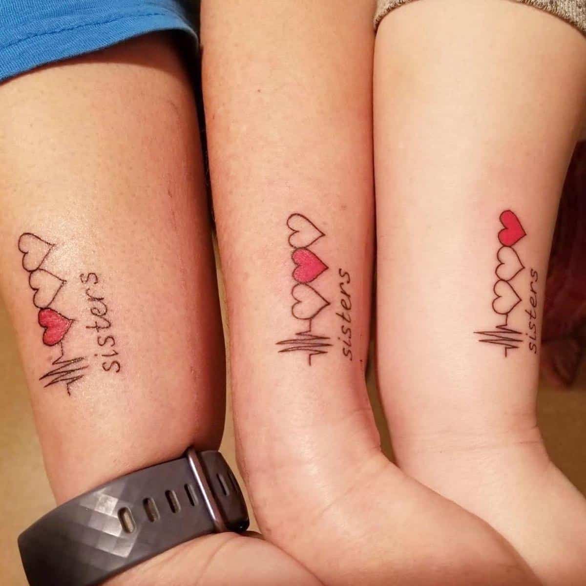 Three arms with matching "sisters" tattoos featuring hearts and heartbeat lines