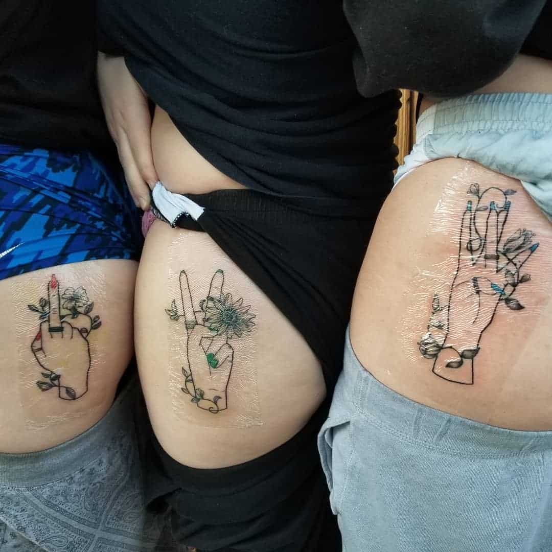 Three thigh tattoos of hands holding flowers and leaves, partially covered in plastic