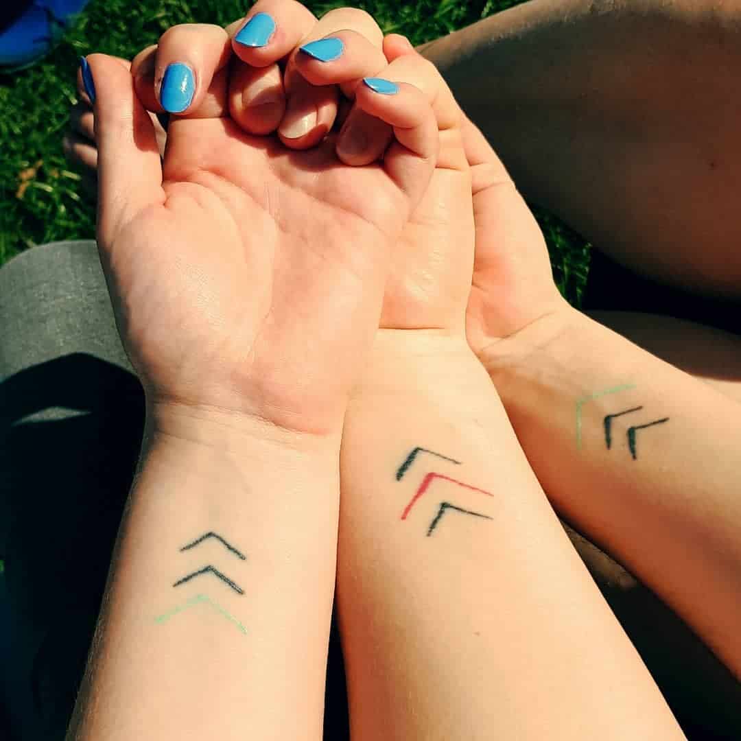 Matching black, green, and red arrow tattoos on two wrists with light blue nails