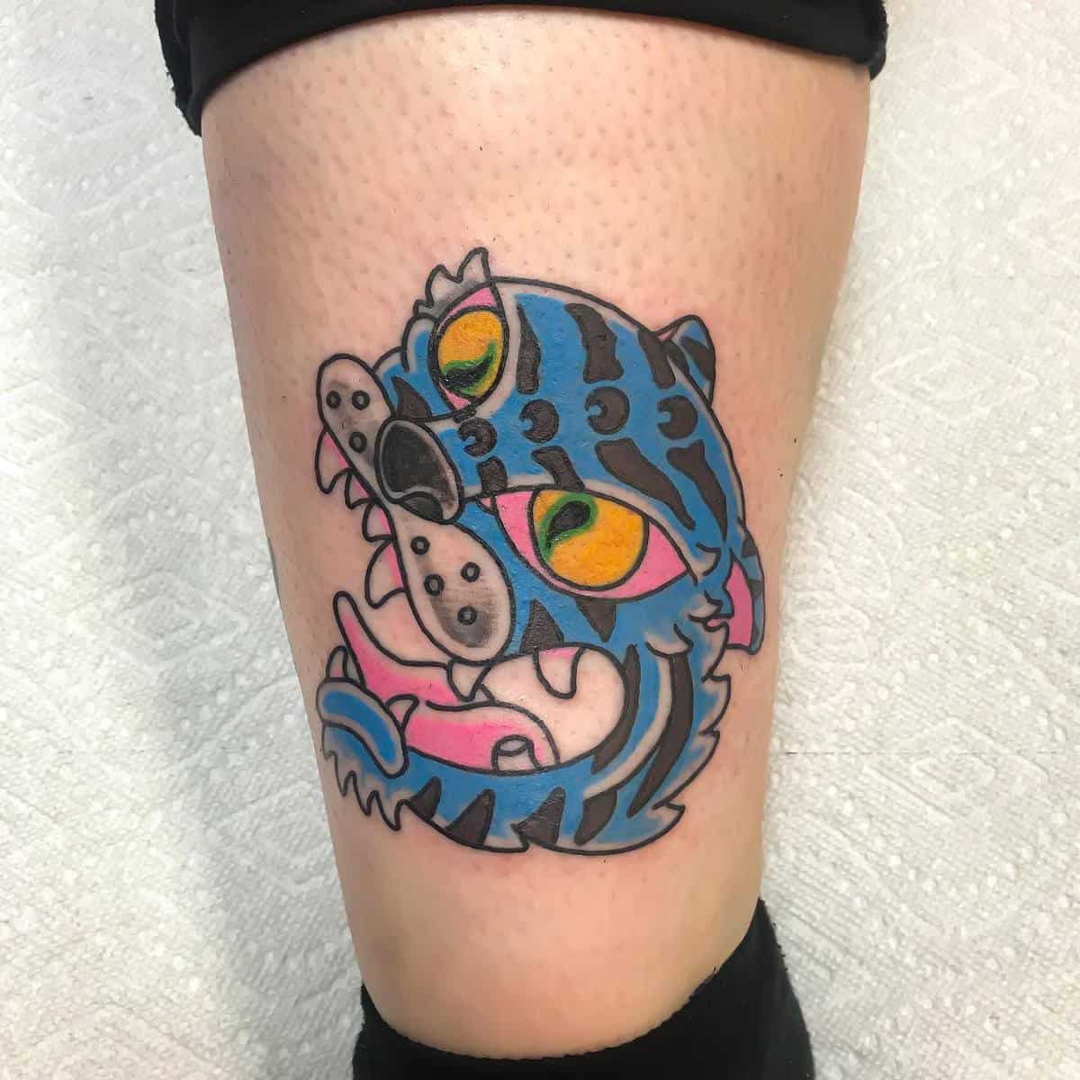 Tattoo of a stylized blue tiger with colorful eyes on the back of a leg