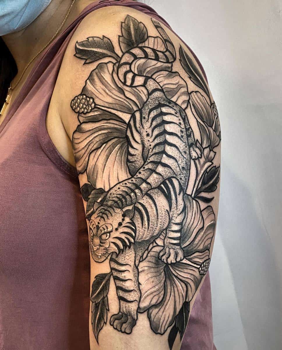 Black and white tiger tattoo surrounded by flowers on an upper arm