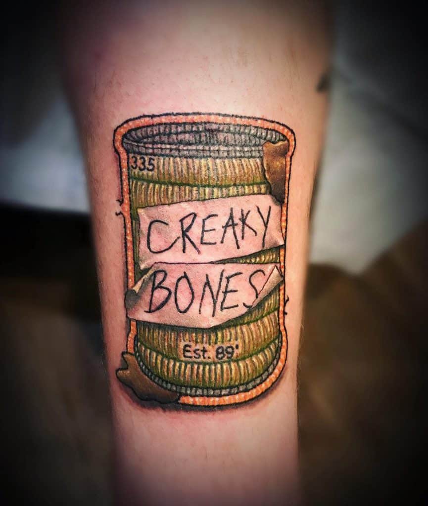 Unique embroidery tattoo of a rusty tin can with 'Creaky Bones' stitched across the label, creating a textured fabric illusion.
