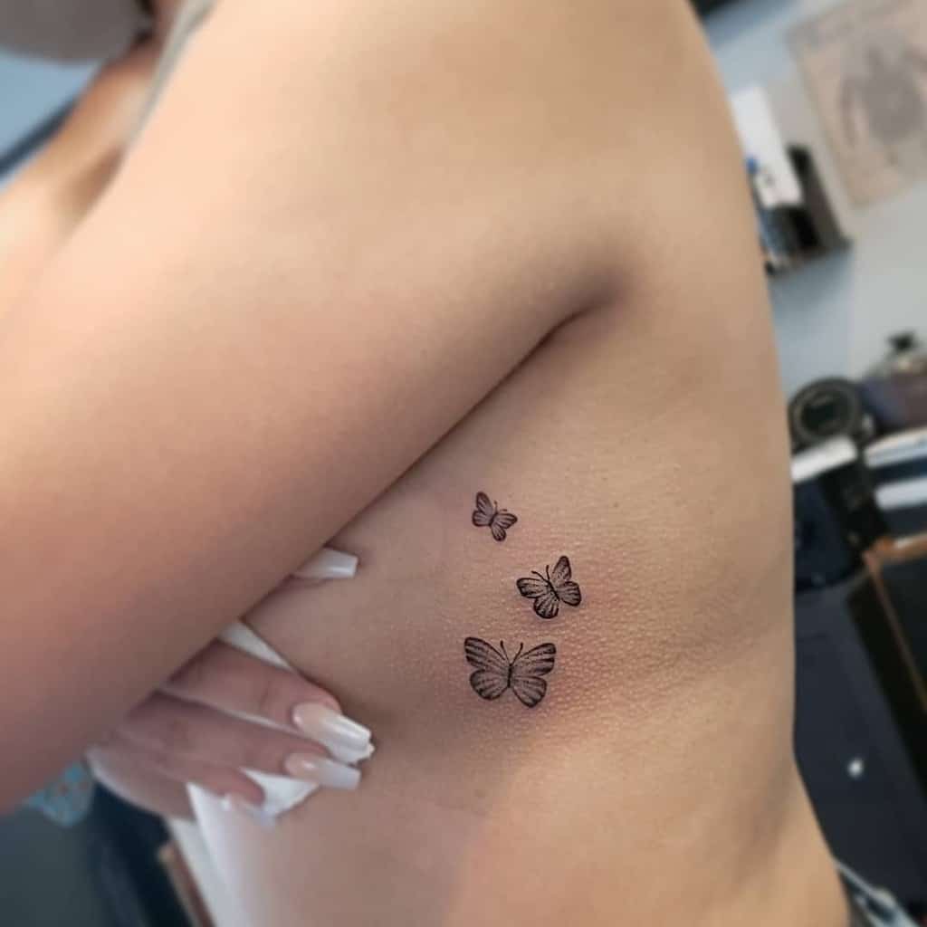 Three black butterfly tattoos grace the ribcage of a woman
