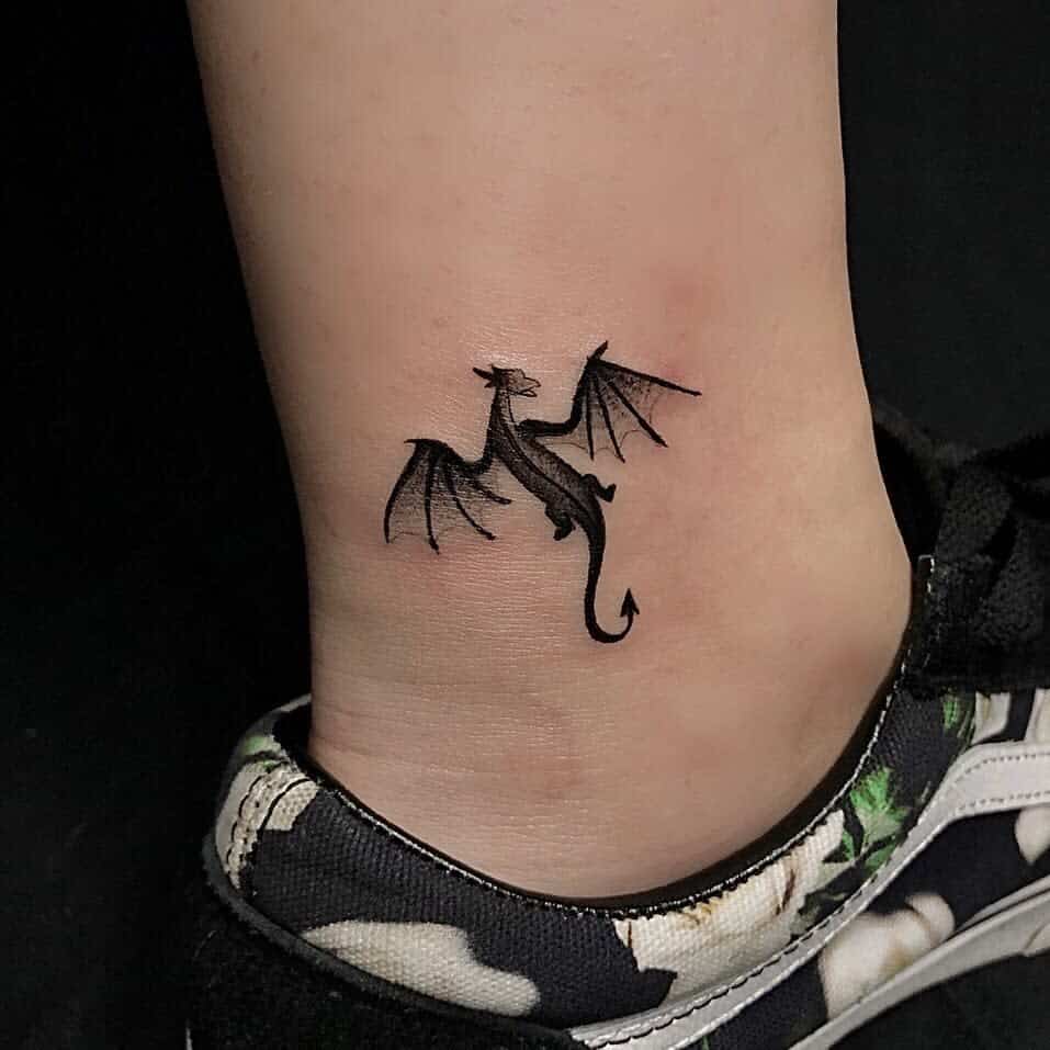 Small black dragon tattoo on an ankle