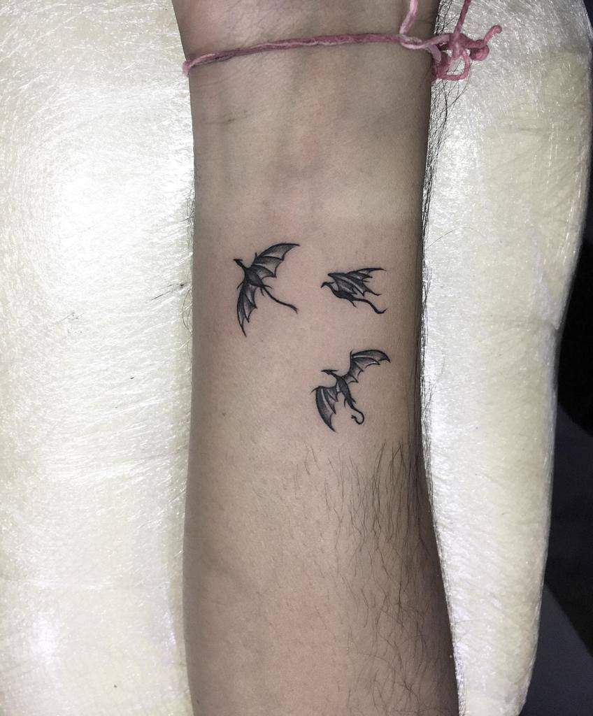 Three small dragon tattoos on a forearm