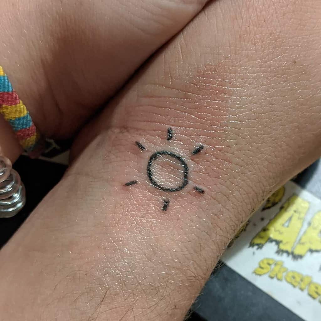 Wrist tattoo of a simple sun design with thin rays extending outward