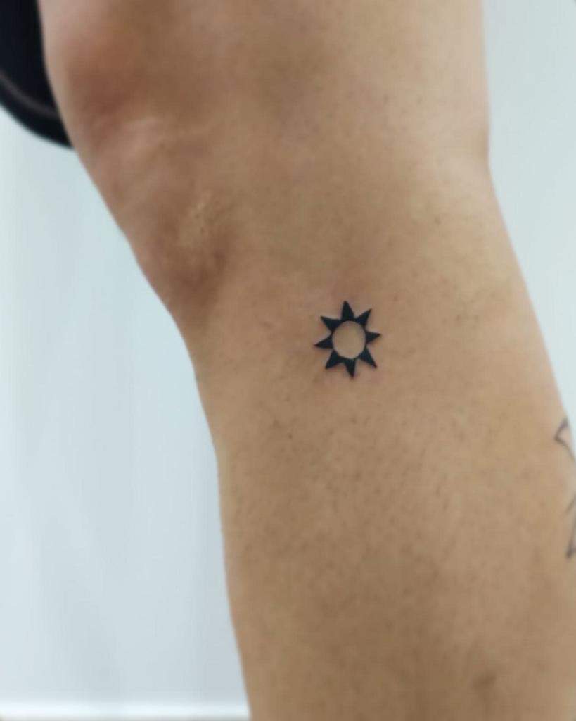 A small tattoo of a sunburst design on the back of a person's leg