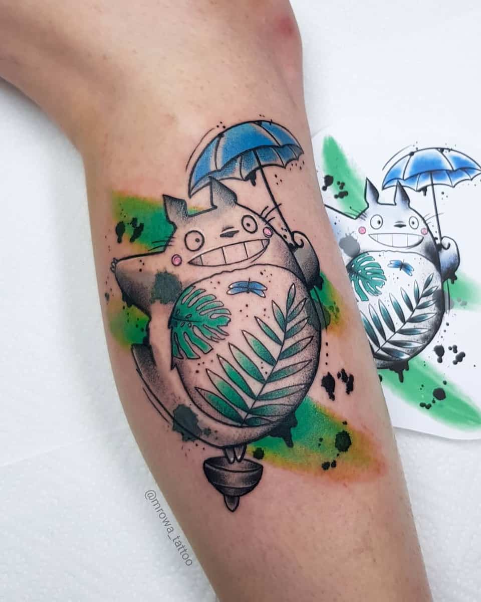 Colorful Totoro tattoo featuring Totoro holding a blue umbrella, with green leaves and artistic paint splashes around it