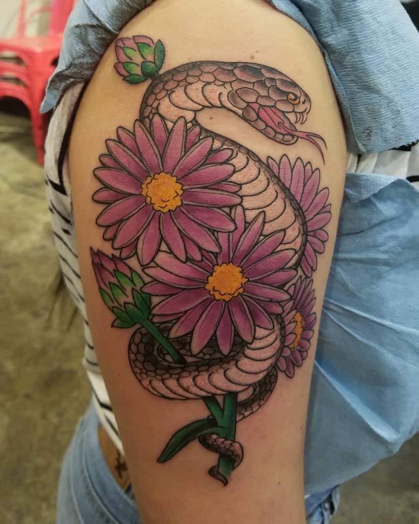 Tattoo of a coiled snake entwined with pink flowers and delicate asters on an upper arm