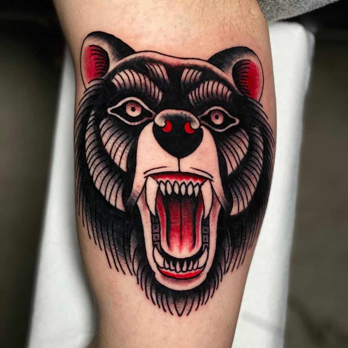 Tattoo of a fierce bear head with an open mouth, red eyes, and sharp teeth emblazoned on a person's arm