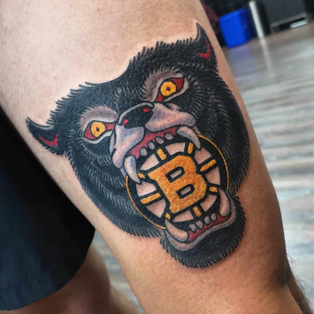 Tattoo of a fierce bear's head biting a circular emblem on a person's thigh