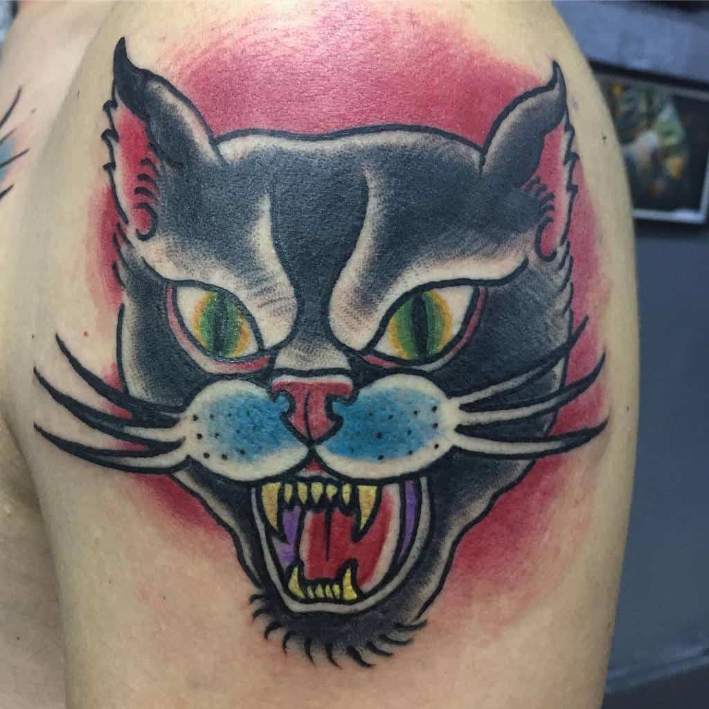 Tattoo of an enraged black cat with vivid, colorful eyes on a person's upper arm