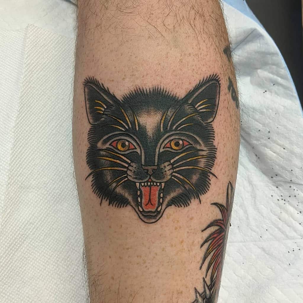 Tattoo of a snarling black cat with piercing orange eyes on a person's forearm