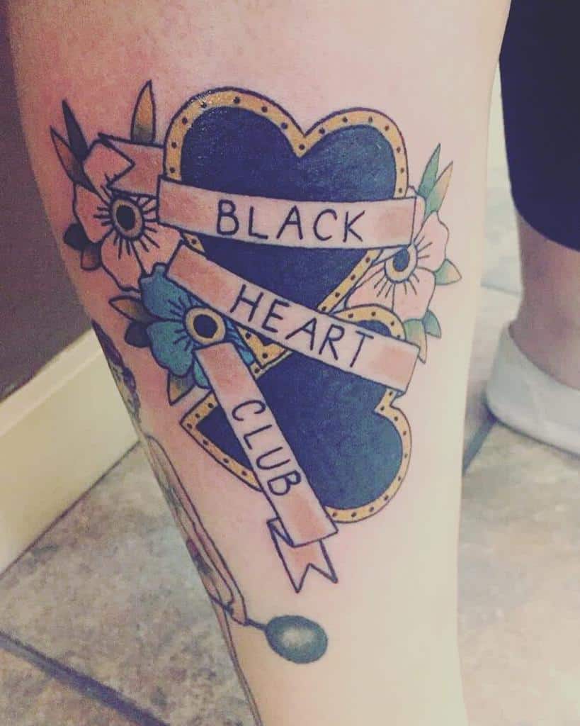 Traditional-style tattoo featuring a black heart with gold trim, floral details, and a banner reading 'Black Heart Club'